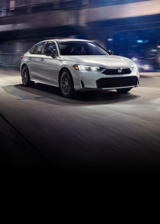 2026 Honda Civic Sedan Sport Touring Hybrid in Solar Silver Metallic front driving on a city street at night (Compact Sedan).